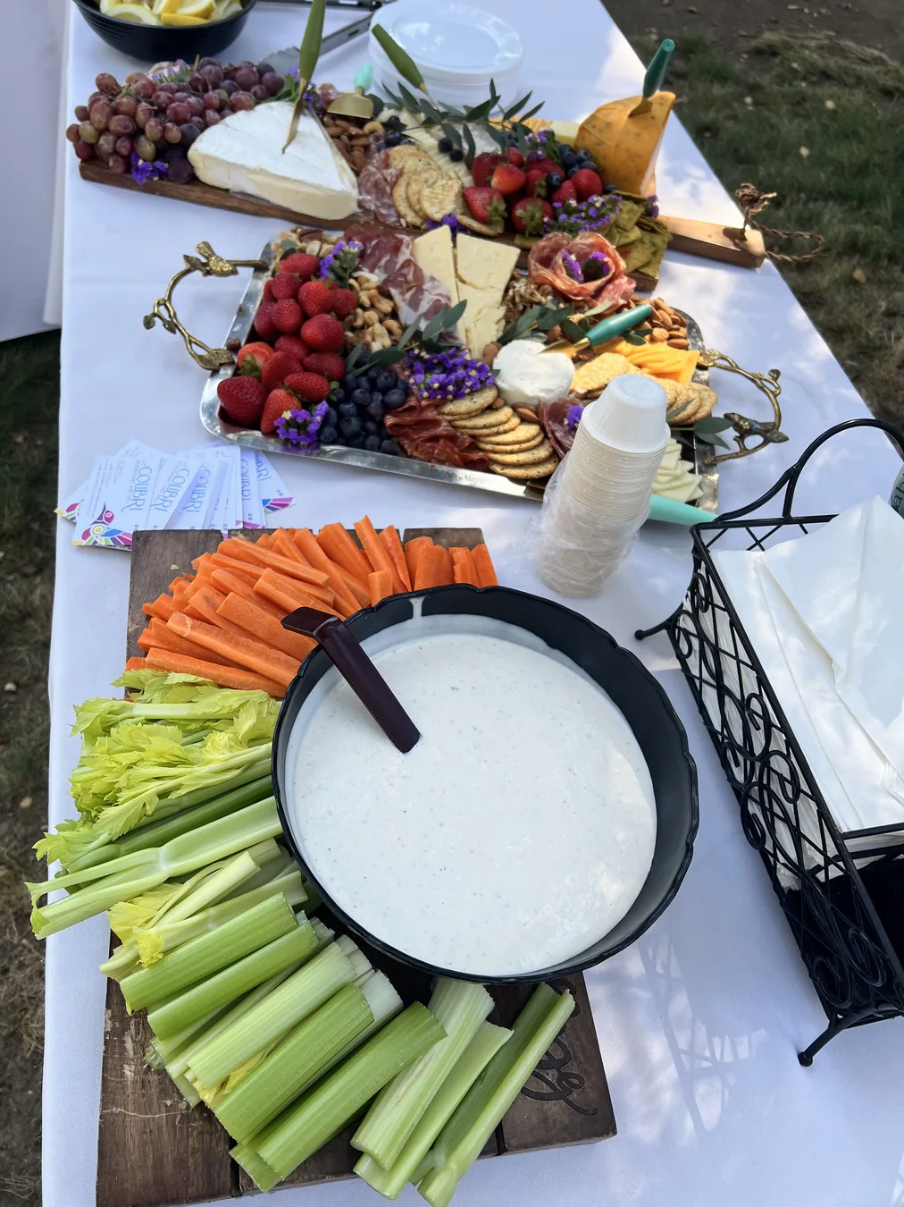 Two El Colibrí grazing boards with brie, cured meats, strawberries, grapes, and crackers beside a veggie tray